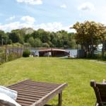 Garten mit Liegestühlen und Blick auf einen See mit Boot.
