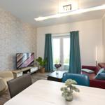 Wohn- und Essbereich mit Sofa, TV und Essplatz. Wand aus Ziegelsteinen und Fenster mit Vorhängen.