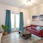Wohnzimmer mit rotem Sofa, Fernseher und Fenster mit grünen Vorhängen.