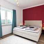Schlafzimmer mit weißem Bett, roter Wand und blauen Vorhängen.
