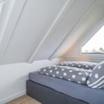 Bedroom with sloped ceiling, windows, and bed with upholstered headboard.
