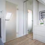 Bedroom with bed, wardrobe, and desk. Wooden floor and sloped ceiling.