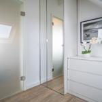 A room with a white dresser, mirror, and glass door. A white orchid sits on the dresser.