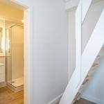 Bathroom with shower and sink. White staircase leads upstairs.