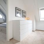 Bedroom with sloped ceiling, white dresser, and windows.