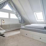 Bedroom with sloped ceiling, bed with drawers, chair, and windows