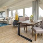 Living and dining area with wooden floor, sofa, table and chairs. Large windows with view.