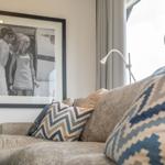 A sofa with cushions near a window and a picture on the wall.