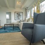 A living room with a gray armchair, sofa, wooden floor, and blue rug.