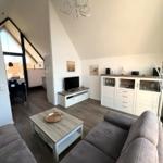 Wohnzimmer mit Sofa, Couchtisch und Fernseher. Blick in die Küche und auf die Terrasse.
