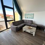 Wohnzimmer mit Ecksofa, Holzboden und großem Fenster mit Blick auf die Umgebung.