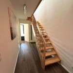 Holztreppe führt zur oberen Etage. Flur mit dunklem Holzboden und Wandbild.