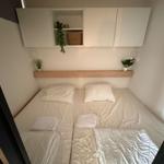 Schlafzimmer mit Bett, weißen Laken und Wandregalen mit Pflanzen.