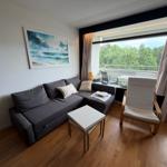 Wohnzimmer mit Sofa, Sessel und Balkon mit Blick auf Bäume.