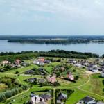 Luftbild einer Wohnsiedlung mit Grünflächen und einem großen See im Hintergrund.