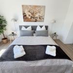 Schlafzimmer mit Bett, Wandbild, Nachttischen und Zimmerpflanze.