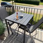 Terrasse mit Tisch, zwei Stühlen, Lampe und Flasche Wein.