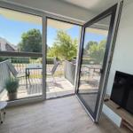 Wohnzimmer mit TV und Balkon. Balkon mit Tisch, Stühlen und Pflanze.