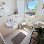 Badezimmer mit Waschbecken, Toilette und Fenster mit Blick nach draußen.