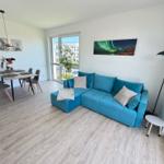 Wohn- und Essbereich mit blauem Sofa, Esstisch und großen Fenstern.