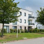 Moderne weiße Wohnhaus mit Balkonen und grünem Gartenbereich.