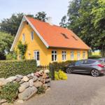 Gelbes Haus mit rotem Dach, umgeben von Bäumen und einem Steinzaun.