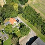 Haus mit rotem Dach, Garten und Parkplatz zwischen Wäldern und Feldern