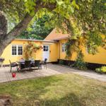 Gelbes Haus mit Terrasse, Grill und Garten. Rote Rosen an der Wand.