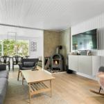 Wohnzimmer mit Kamin, Fernseher und großem Fensterblick auf Wald