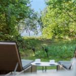 Zwei Liegestühle und Tisch auf Terrasse mit Blick durch Bäume zum See.