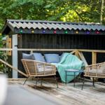 Terrasse mit Sitzgelegenheit vor einem Holzschuppen mit bunten Lichterketten.