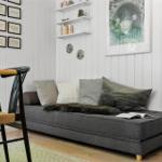 Ein grauer Sofa mit Kissen und Fell liegt in einem Raum mit weißen Wänden und einem Stuhl.