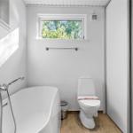 Badezimmer mit Badewanne, Toilette und Fenster zum Wald.