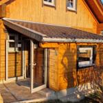 Holzhaus mit Eingangstür und Veranda. Außenbereich mit Bank und Steinpflaster.