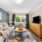 Wohnzimmer mit Sofa, Fernseher und Fenster mit Blick auf Grün.