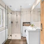 Badezimmer mit Dusche, Waschmaschine und Fenster mit Blick auf Grün.