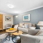 Wohnzimmer mit Sofa, Sesseln, Tisch und Wandbildern.