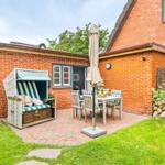 Roter Backsteinbau mit Terrasse, Strandkorb und Garten. Tisch mit Stühlen und geschlossener Sonnenschirm.