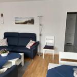 Wohnzimmer mit Sofa, Tisch und Stühlen. Durchgang zu Küche und Flur.