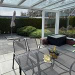 Terrasse mit Tisch, Stühlen und Sonnenschirm unter Glasdach.