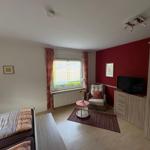 Ein Zimmer mit Bett, Sessel, Fernseher und Fenster mit Blick auf Garten.