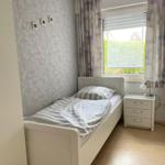 Ein Schlafzimmer mit einem Bett, Nachttisch und Fenster mit Vorhängen.