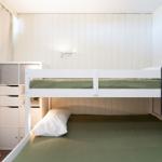 Ein Doppelstockbett mit grüner Bettwäsche und weißer Matratze. An der Wand hängt eine Wandlampe.