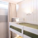 Schlafzimmer mit Doppelstockbett, Wandlampe und Fenster mit Vorhang.