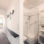Badezimmer mit Dusche und Waschbecken. Flur mit Schrank und Blick auf Balkon.