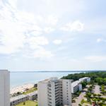 Panoramablick auf Strand, See und Wohnhäuser unter blauem Himmel mit weißen Wolken.