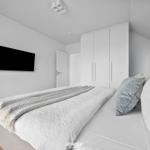 Schlafzimmer mit Bett, Kleiderschrank und Wandfernseher.