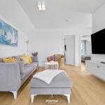 Wohnzimmer mit grauem Sofa, Fernseher und Wandbild mit Segelbooten.