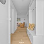 Flur mit weißer Wand und Sitzbank mit Kissen. Holzdielenboden und Blick in Wohnzimmer.