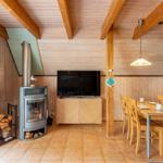 Wohn- und Essbereich mit Holzvertäfelung, Kaminofen, TV und Tisch mit Stühlen.